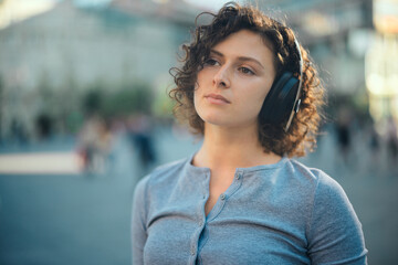 Fototapeta premium Portrait of a young woman standing in the city square and listening to music.