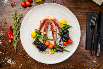 Octopus with black risotto. Carrot cream, mini-broccoli, basil pesto. Delicious healthy traditional food closeup served for lunch in modern gourmet cuisine restaurant - 447876927
