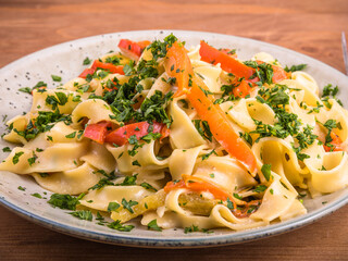 Portion of traditional italian fettuccine pasta with bell pepper sauce sprinkled with parsley on a plate on a wooden table, close-up