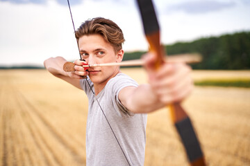 Young male sportsman targeting with traditional bow - Teenager archer practicing archery in nature - Outdoors sports and recreation concept with a millennial boy - obrazy, fototapety, plakaty