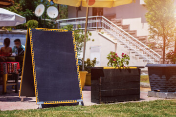 Empty food chalkboard with space for mockup stands on grass near street cafe