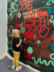 oung blonde caucasian child painting a graffiti on the wall with red spray