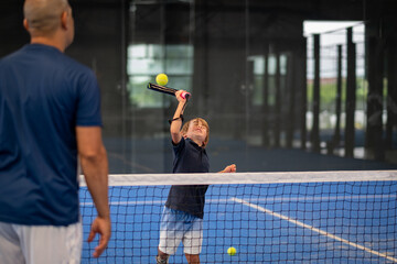 Monitor teaching padel class to child, his student - Trainer teaches little boy how to play padel on indoor tennis court