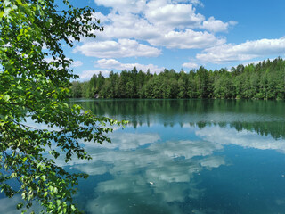 The shore of the lake Light with turquoise water, which reflects the trees and the sky with clouds, in the mountain park Ruskeala.