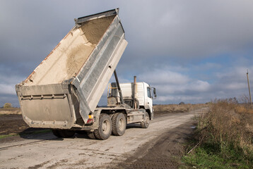 dump truck with a raised body on a dirt road. The process of transportation and unloading of soil on construction equipment. Commercial vehicles