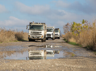 three dump trucks drive one after another on a dirt road after rain. The process of transportation...