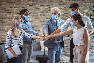 Group of colleagues wearing protective face masks and fist bumping while having business meeting during coronavirus pandemic. United business team during coronavirus pandemic!