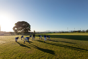 Diverse group of female baseball players with coach warming up in sunny field, stretching