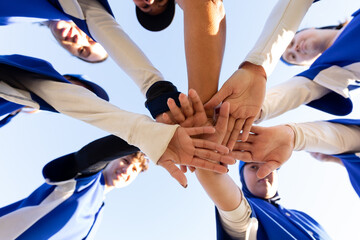 Diverse group of happy female baseball players stacking hands on sunny baseball field before game