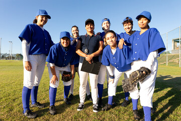 Portrait of diverse group of smiling female baseball players and coach standing on sunny field