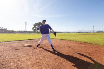 Mixed race female baseball player on sunny baseball field throwing ball during game