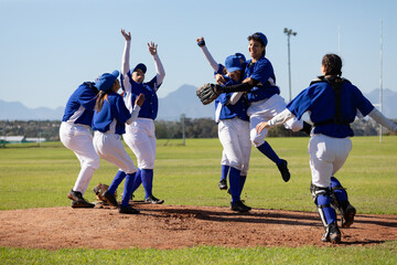 Diverse group of happy female baseball players celebrating on sunny baseball field after game