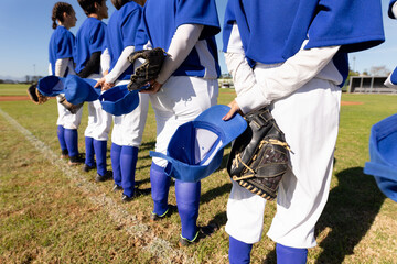 Diverse group of female baseball players standing on field with hands behind backs before game