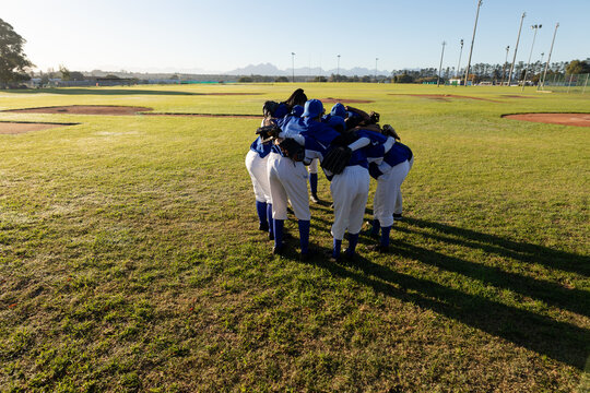 Diverse group of female baseball players standing in huddle on baseball field