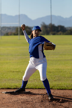 Mixed race female baseball pitcher on sunny baseball field throwing ball during game