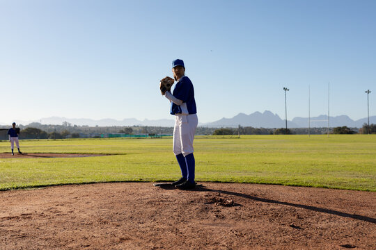 Mixed race female baseball pitcher on sunny baseball field preparing to throw ball during game