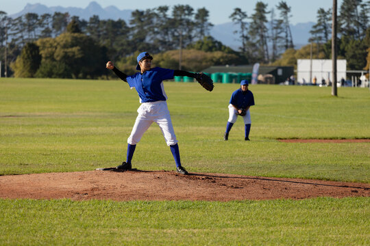 Mixed race female baseball pitcher on sunny baseball field throwing ball during game
