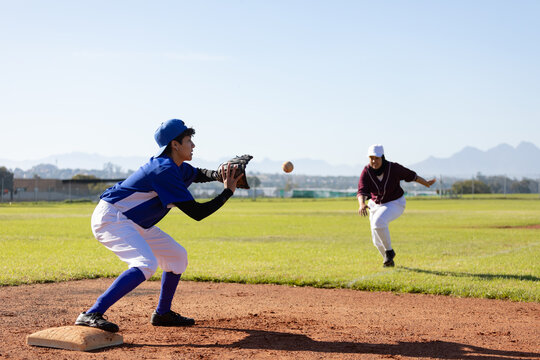 Mixed race female baseball player on sunny baseball field reaching to catch ball during game