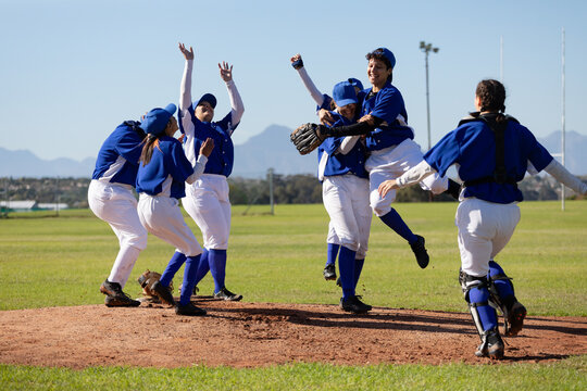 Diverse group of happy female baseball players celebrating on sunny baseball field after game