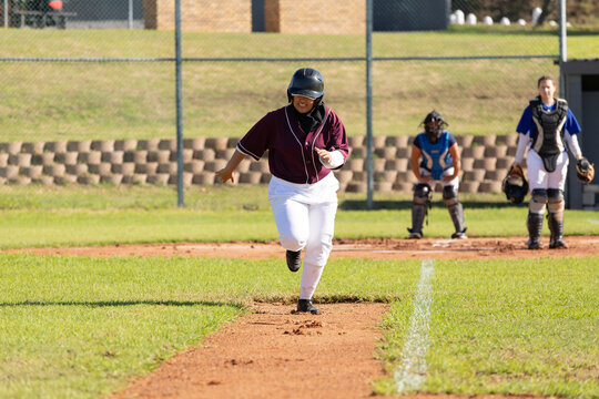 Mixed race female baseball player on sunny baseball field running between bases during game
