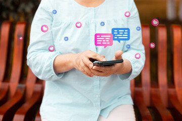 Cropped shot of smiling young woman using her mobile phone, reading messages on mobile phone in a city park
