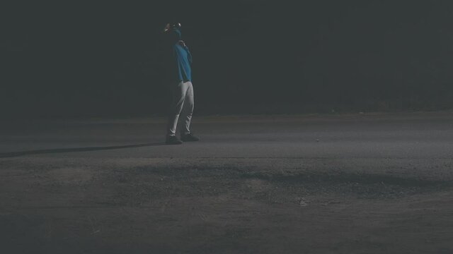 Silhouette of a drunk man in a cowboy hat is walking along the night roadway. Then the man takes a sip of alcohol from the can and casually throws the empty can on the track