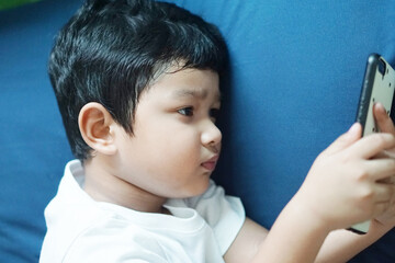 Obraz premium Cute little Asian 4 year old baby boy child watching a video from smart phone. Kids playing with mobile phone. leisure children technology and internet addiction concept. 