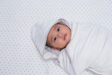 Half body portrait of a baby girl wrapped in white towel after bathing, lying down on bed. 