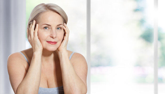 Beautiful middle-aged blonde woman sitting relaxed near the window. Selective focus on face. Realistic images with their own imperfections.
