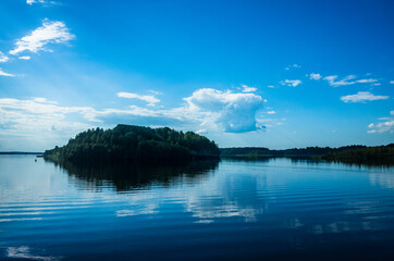 Small island covered with trees among the lake. Beautiful blue sky with clouds and water using for background. The sky is reflected in the water.