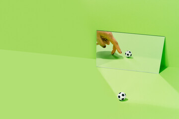Hand of an unknown woman playing with a soccer ball on a green background with a mirror. football and sport concept.