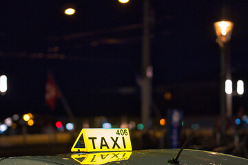 Shallow focus of yellow sign of taxi on top of car at nigh with blurred lights in the background