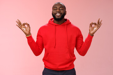 Happy african american bearded man in red hoodie meditating found peace nirvana smiling delighted...
