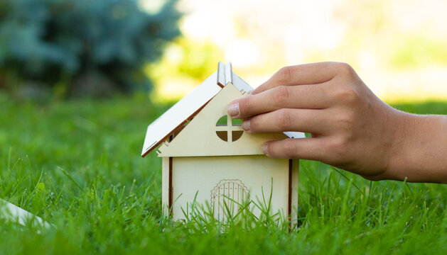 The child collects a mock-up of a wooden house on the green grass. Close-up of hands. Family values. A house built by your own hands. Place for your text.