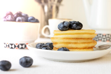 Freshly cooked delicious pancakes stacked on a white plate, served with fresh blueberries, close-up.