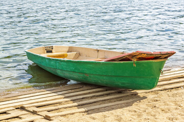 Naklejka premium Empty shabby plastic boat for river walks stands on the shore of the pond