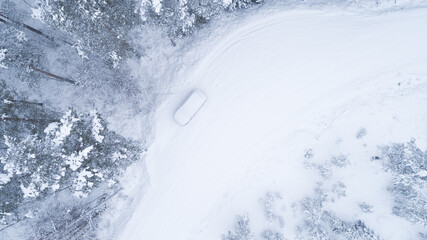 Aerial view of vehicle covered with snow in the winter blizzard in the forest. Car accident. Danger weather.