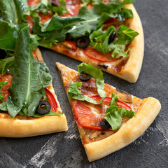 Vitamin Italian pizza with herbs and vegetables. Close-up shot. Sliced vegetarian pizza with spinach, tomatoes and olives. Soft focus.