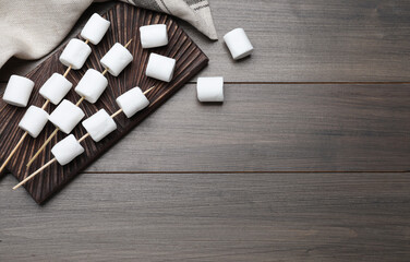 Obraz premium Sticks with marshmallows on wooden table, flat lay. Space for text