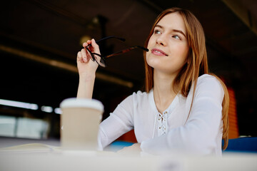 Contemplative female student with optical spectacles in hand thoughtful looking away and thinking...