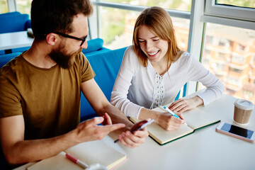 Obraz premium Funny hipster guys learning and studying together discussing publication idea in coffee shop, happy male and female friends communicate about education while browsing website on modern smartphone