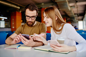 Young hipster guys learning and studying together discussing publication idea in coffee shop,millennial male and female friends communicate about education while browsing website on modern smartphones