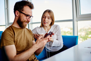 Caucasian hipster guy browsing web publication on modern cellphone technology using 4g wireless during friendly meeting with millennial female blogger, young man reading received email message