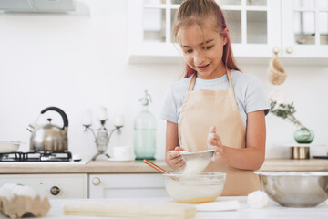 Portrait of a little blonde teen girl wearing apron in kitchen