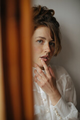 Woman with brunette hair in transparent outfit looking into camera in apartment. Lady in white clothes with freckles posing inside..