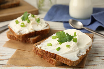 Bread with cream cheese, green onion and parsley on white wooden table, closeup