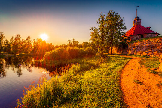 Medieval fortress on the river bank. Sunset. Woodland. Blue sky. The road near the fortress wall. Beautiful nature. Korela Fortress, Priozersk, Russia. View from the side of the road.