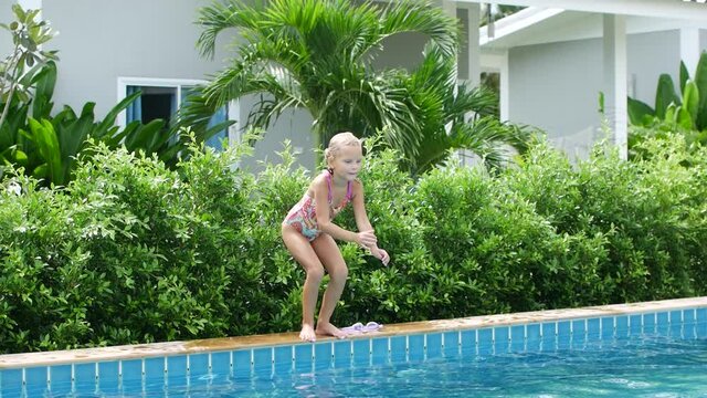 6 year old girl in a swimsuit jumps into the pool, resort in Thailand