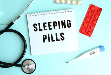 The text SLEEPING PILLS is written on a white notepad that lies next to the stethoscope and pills...