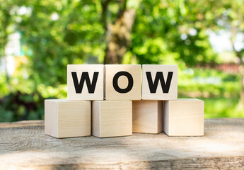 Three wooden cubes are stacked in the WOW word. They lie on other cubes against the backdrop of the summer garden.